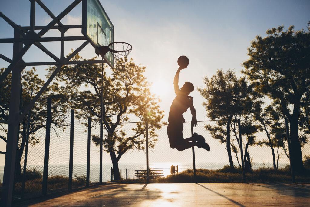 black man doing sports, playing basketball on sunrise, jumping silhouette